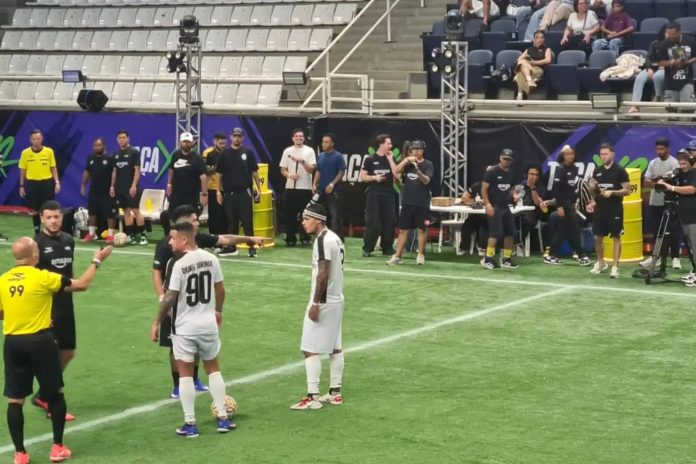 Disputa de jogo de futebol com influenciadores digitais em campo, com árbitro e equipes, em evento realizado no Ginásio José Liberatti, Osasco.