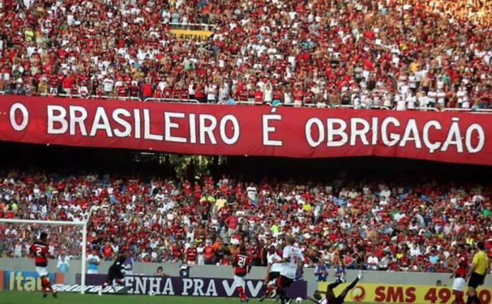 expresso-37c68232b23be94214cc9f51 Torcida do Flamengo exibe faixa com a frase "Brasileirão é obrigação" durante jogo, simbolizando a pressão e expectativa quanto ao título nacional.