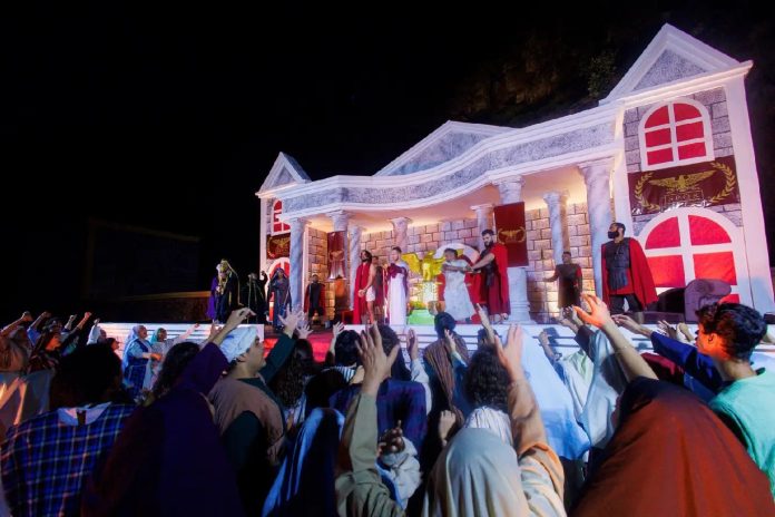 Cena dos ensaios do espetáculo Paixão de Cristo em Itapevi, com montagem cenográfica que retrata arquitetura romana e atores vestidos com trajes históricos em espaço aberto, iluminado para apresentação teatral noturna.