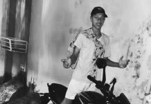 Adolescente de 16 anos morre após conflito familiar em Itapevi Fotografia em preto e branco de um adolescente posando em frente a uma parede, com uma motocicleta visível parcialmente. Imagem vinculada a redes sociais, usada para identificação do jovem falecido e tratada como foto de arquivo.