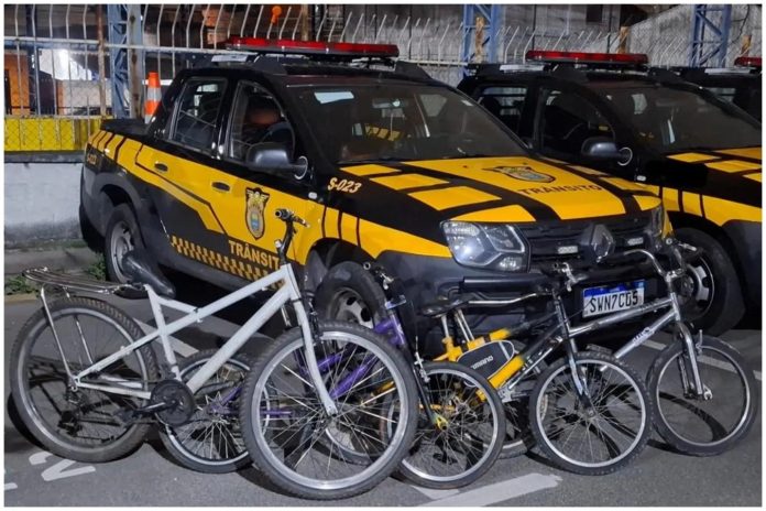 expresso-444b2b7ce137055c396f486e Bicicletas recolhidas em operação de fiscalização contra a prática proibida de 'pegar rabeira' em Barueri, com viaturas da Secretaria de Mobilidade Urbana ao fundo