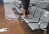 Chuva Intensa Causa Inundações e Danos em Paulicéia, SP Área interna alagada na unidade de saúde em Paulicéia durante forte tempestade, com água cobrindo o chão e pessoa em cima das cadeiras para evitar contato com a água.