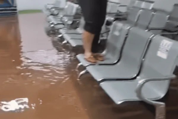 expresso-466d37971c84aed39c9a5509 Área interna alagada na unidade de saúde em Paulicéia durante forte tempestade, com água cobrindo o chão e pessoa em cima das cadeiras para evitar contato com a água.
