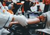 SESI Carapicuíba promove ação de doação de sangue em parceria com Amor se Doa Pessoa doando sangue em ambiente coletivo, mostrando preparação para coleta com profissional de saúde usando luvas.