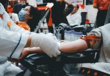 SESI Carapicuíba promove ação de doação de sangue em parceria com Amor se Doa Pessoa doando sangue em ambiente coletivo, mostrando preparação para coleta com profissional de saúde usando luvas.