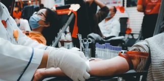 SESI Carapicuíba promove ação de doação de sangue em parceria com Amor se Doa Pessoa doando sangue em ambiente coletivo, mostrando preparação para coleta com profissional de saúde usando luvas.