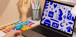 Carapicuíba lança oficina gratuita de design gráfico com inscrições online Mãos utilizando mesa digitalizadora gráfica, computador com ilustrações e paleta de cores, em ambiente de trabalho de design gráfico.