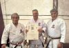 Gilberto Schavareto Jr. é homenageado internacionalmente com título honorífico em karatê Gilberto de Mello Schavareto Junior, técnico de karatê de Osasco, segurando o certificado do título Renshi Shihan concedido pela IKGA, ao lado de dois mestres durante a cerimônia em Cartagena, Colômbia.