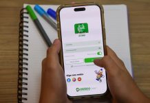 Famílias de Osasco Ganham Aplicativo para Acompanhar Vida Escolar dos Alunos Pessoa segurando um celular com a tela de login do aplicativo Portal do Aluno da Prefeitura de Osasco, sobre uma mesa com caderno e canetas.