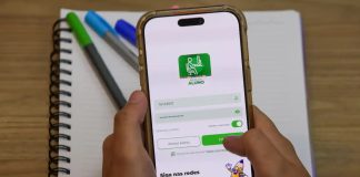 Famílias de Osasco Ganham Aplicativo para Acompanhar Vida Escolar dos Alunos Pessoa segurando um celular com a tela de login do aplicativo Portal do Aluno da Prefeitura de Osasco, sobre uma mesa com caderno e canetas.