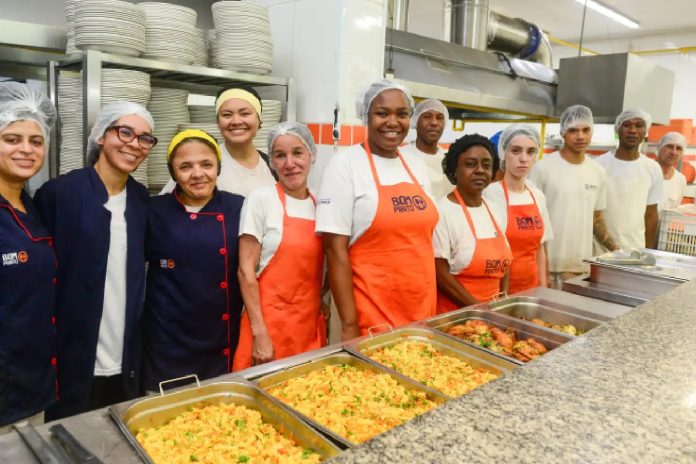 Equipe de funcionários do Bom Prato posando na cozinha, com travessas de comida à frente