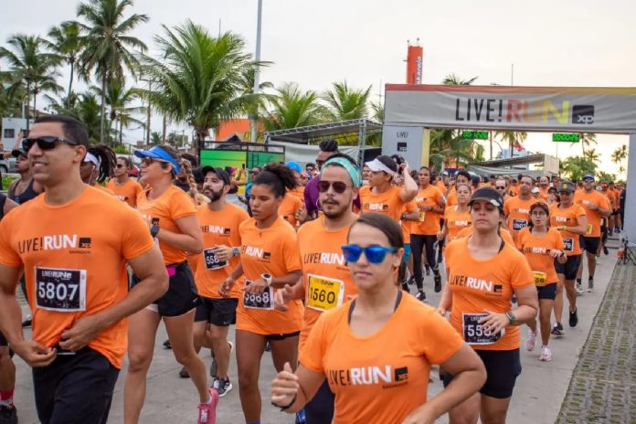 expresso-f22f85e5217543234761fe78 Participantes da LIVE! RUN XP usando camisetas laranja durante corrida, com faixa de largada ao fundo exibindo logo do evento